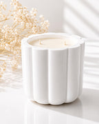 White candle in a decorative holder with light filtering through, on a white surface.