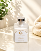 White diffuser bottle with gold label on a light surface with a plant in the background